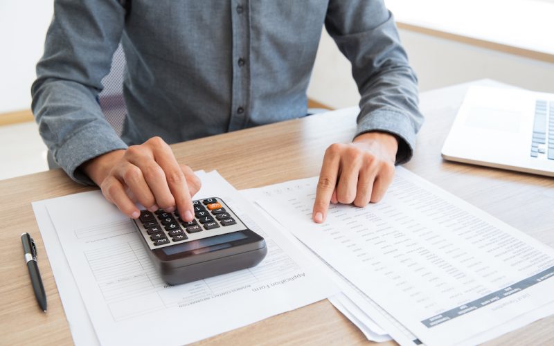 Close-up of unrecognizable man working with financial data. He using calculator and examining document. Financial inspector holding examination. Paperwork or finance concept